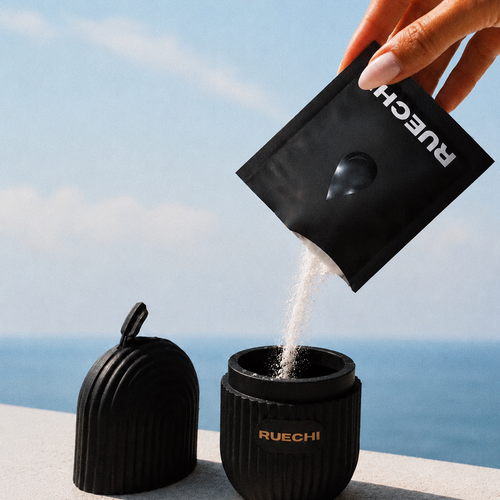 Person pouring a white substance from a RUECHI package into a black container with a scenic background.